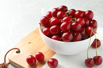 Photo of Wooden board with bowl of tasty ripe cherries on light table