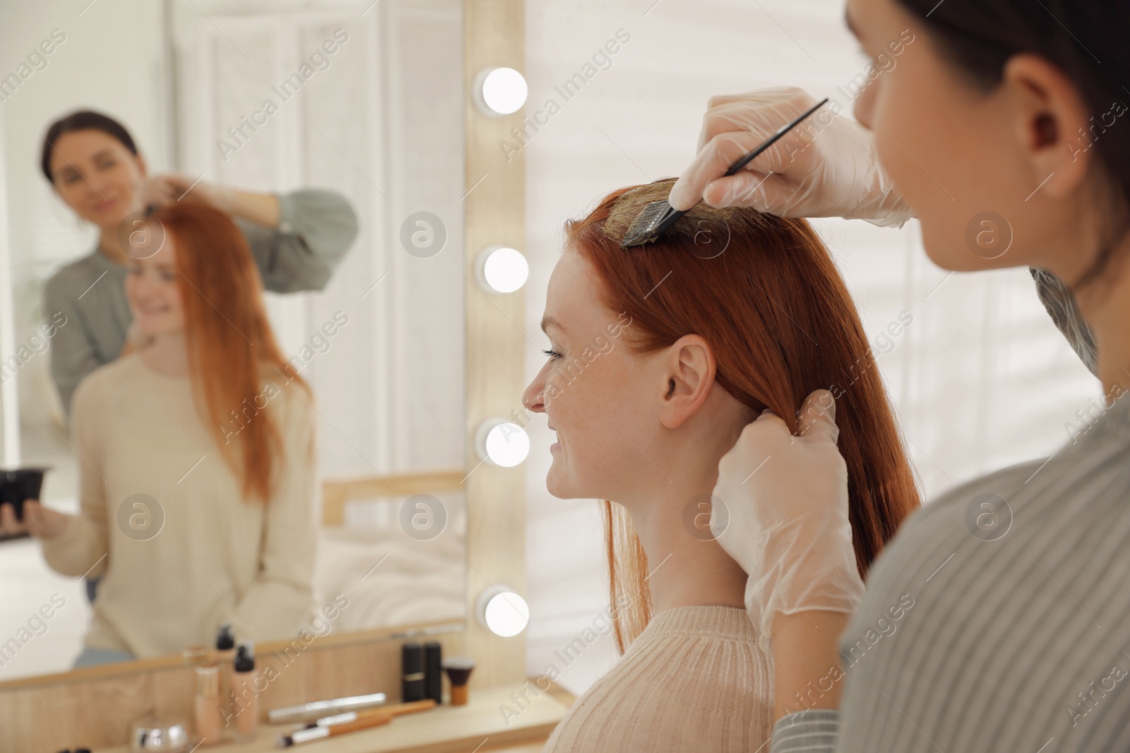 Photo of Professional hairdresser dyeing woman's hair with henna in beauty salon, space for text