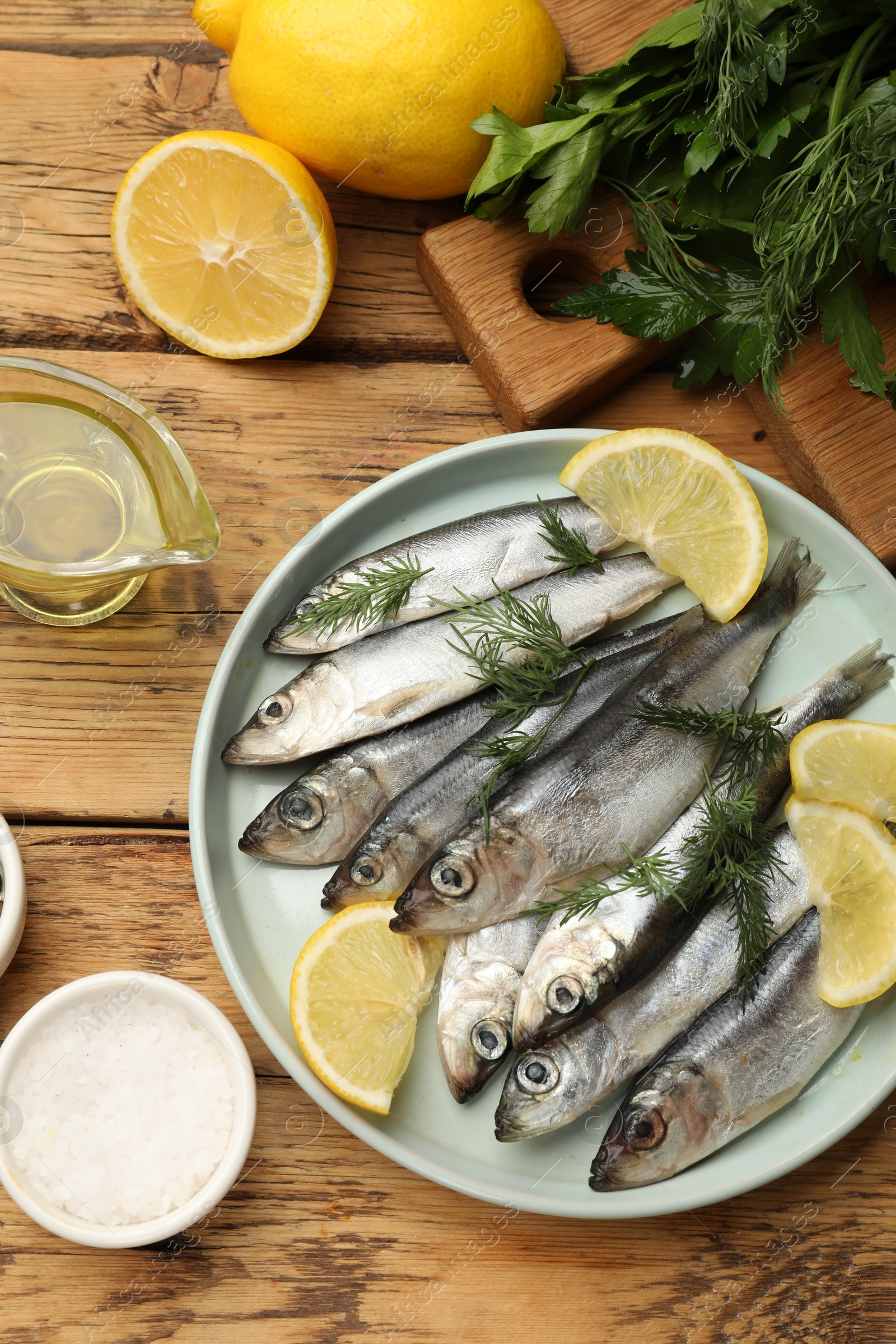 Photo of Fresh raw sprats, lemon and dill on wooden table, flat lay