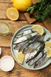 Photo of Fresh raw sprats, lemon and dill on wooden table, flat lay