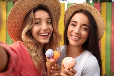 Photo of Young women with ice cream taking selfie outdoors