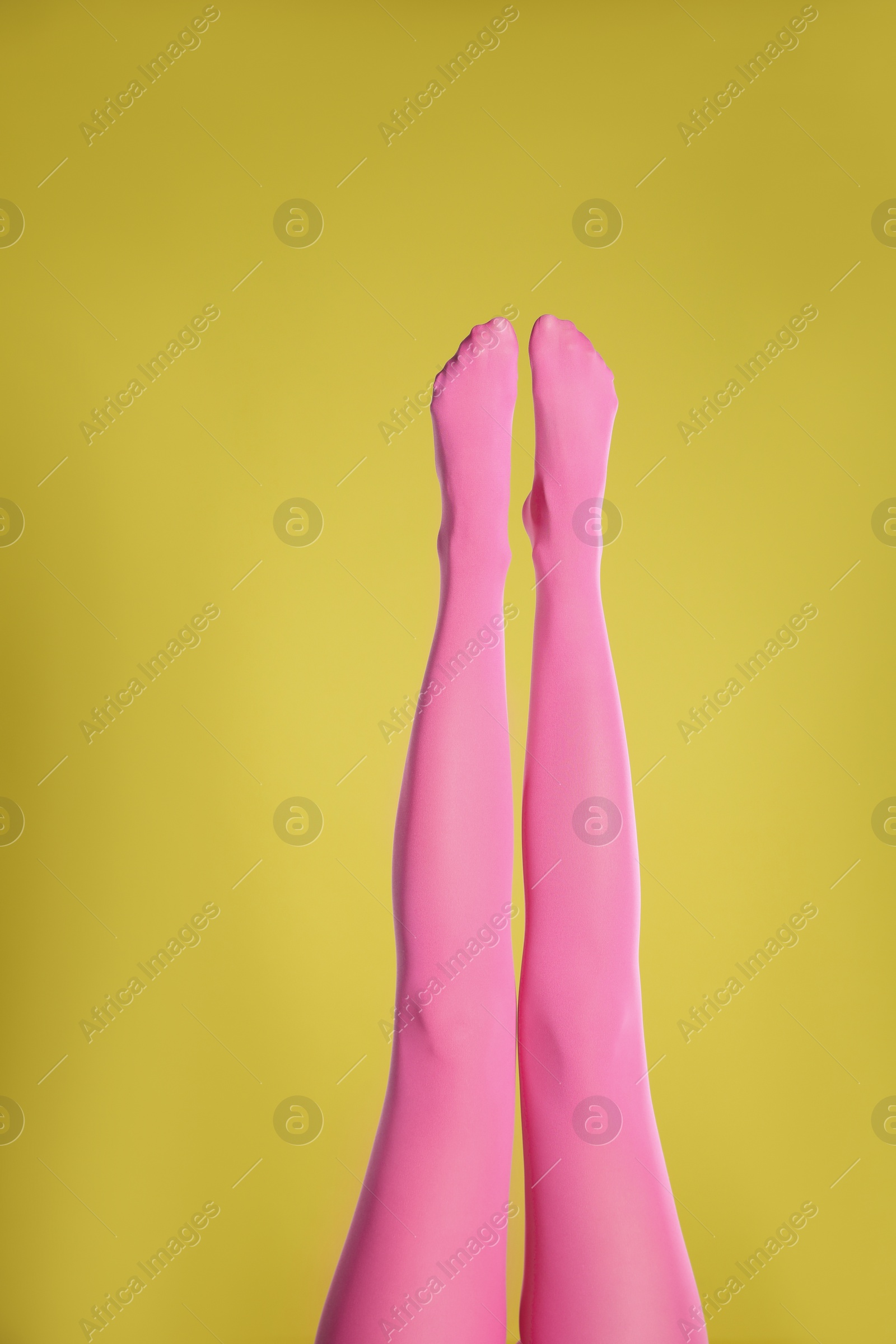 Photo of Woman wearing pink tights on yellow background, closeup of legs