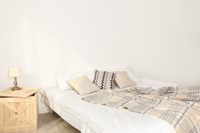 Bed with pillows and plaid in modern room interior