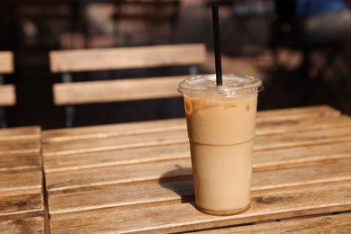 Photo of Takeaway plastic cup with cold coffee drink and straw on wooden table outdoors, space for text
