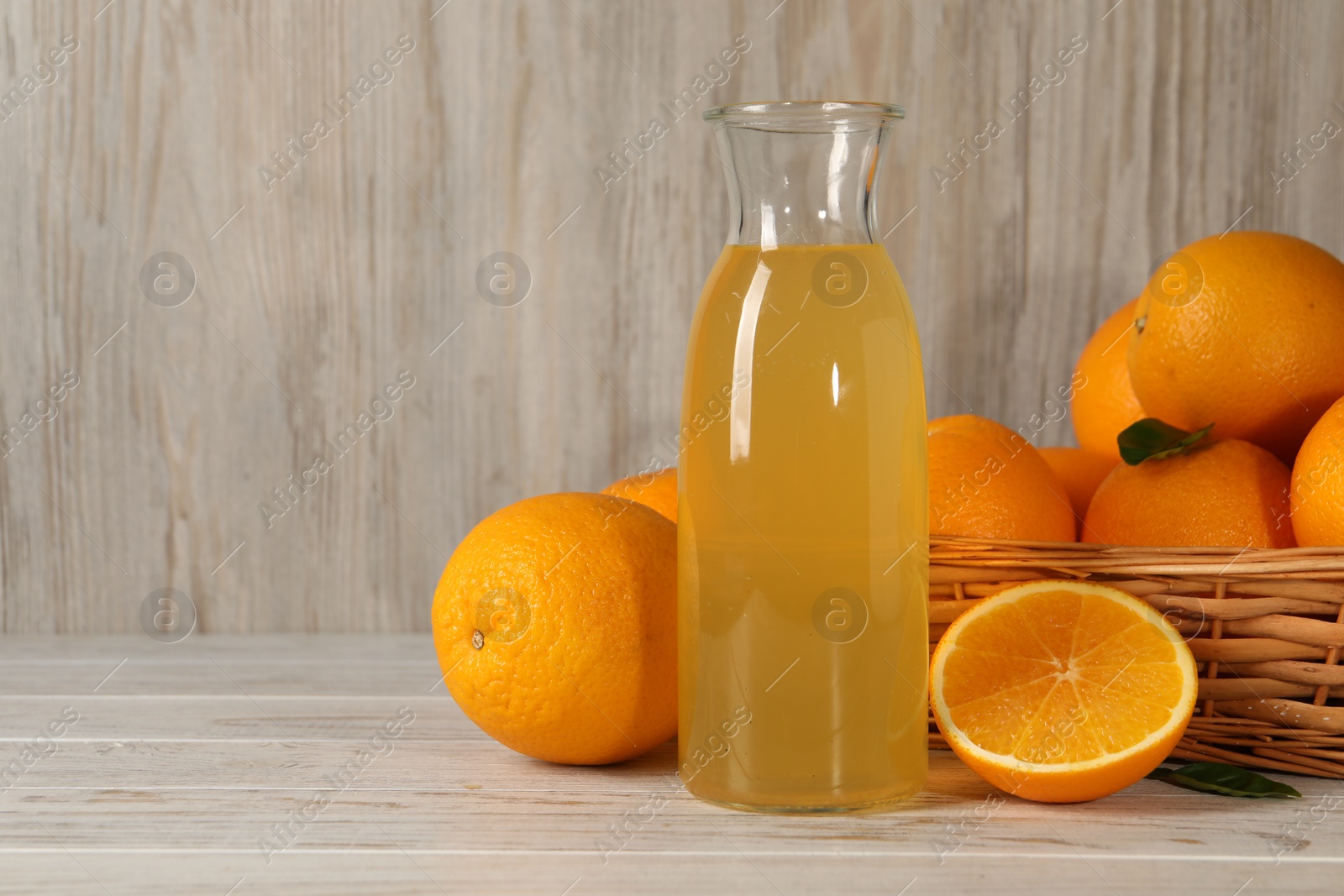 Photo of Many ripe oranges and fresh juice on light wooden table, space for text