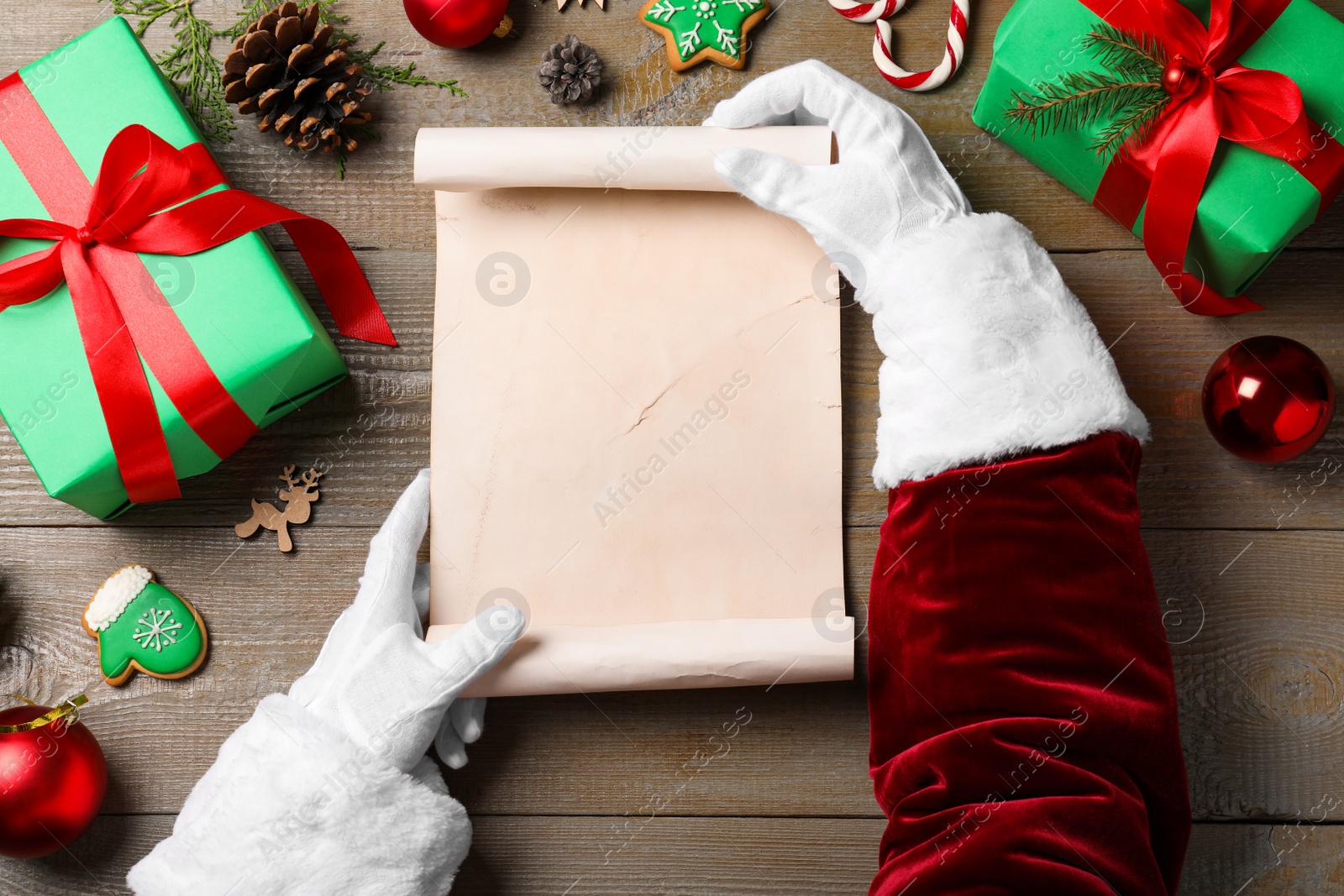 Photo of Santa Claus holding empty paper at wooden table, top view. Space for text