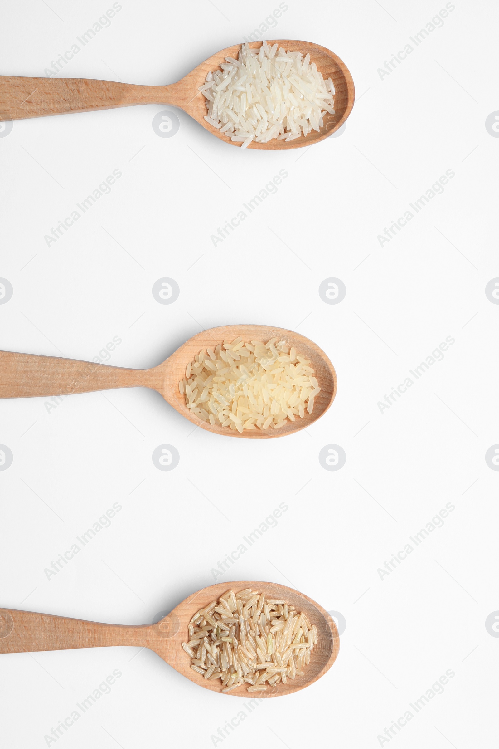 Photo of Spoons with different types of uncooked rice on white background, top view