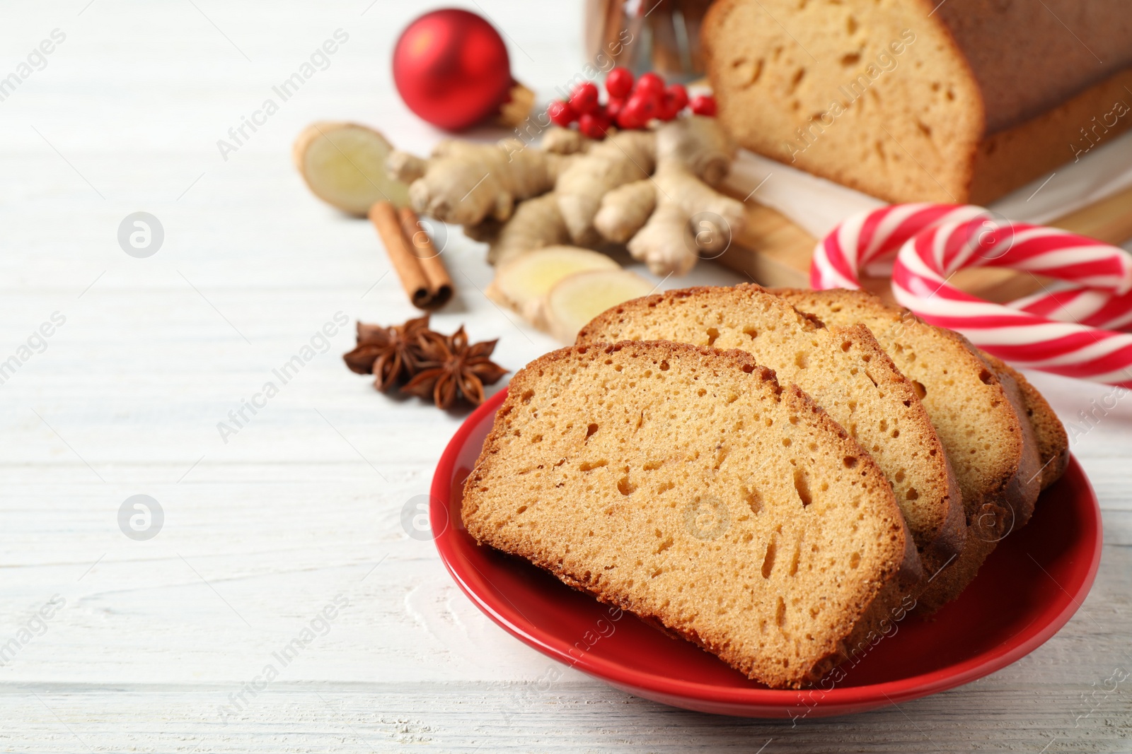 Photo of Slices of delicious gingerbread cake, ingredients and candy canes on white wooden table. Space for text