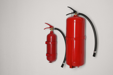 Photo of Different fire extinguishers hanging on white wall. Space for text