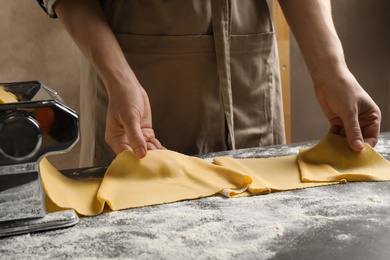 Woman preparing dough with pasta maker machine at grey table, closeup