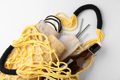 Photo of Fishnet bag with different items on white background, top view. Conscious consumption