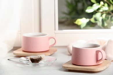 Photo of Cups of hot tea with wooden coasters on window sill