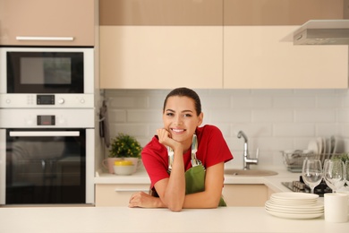 Beautiful young woman with clean dishes in kitchen