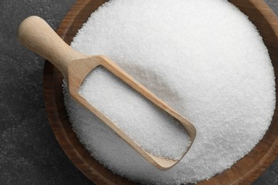 Granulated sugar in bowl and scoop on grey textured table, top view