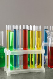 Photo of Test tubes with liquids in stand on table against light grey background, closeup