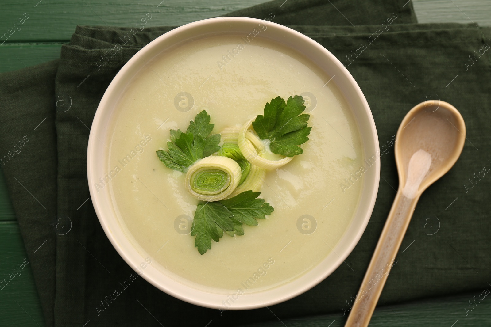 Photo of Delicious leek soup served on green wooden table, top view