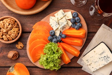Photo of Delicious persimmon, blue cheese and blueberries on wooden table, flat lay