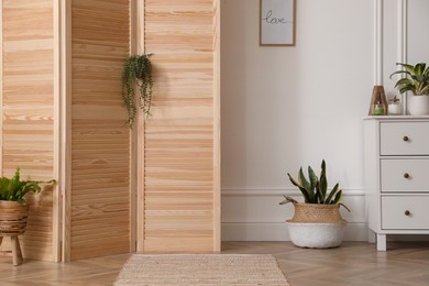 Stylish room with wooden folding screen and chest of drawers near white wall. Interior design