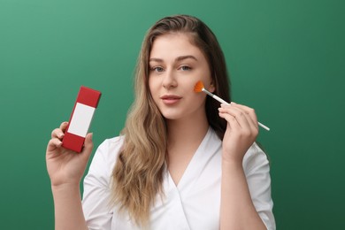 Cosmetologist with cosmetic product and brush on green background