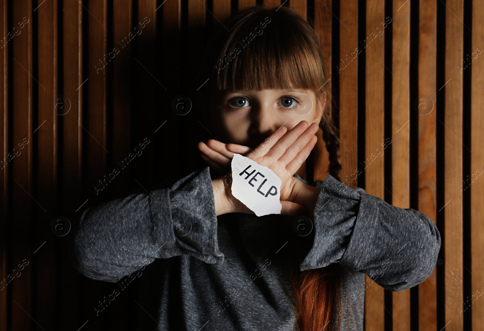 Photo of Sad little girl with sign HELP on wooden background. Child in danger