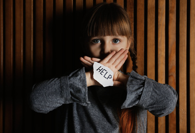 Photo of Sad little girl with sign HELP on wooden background. Child in danger