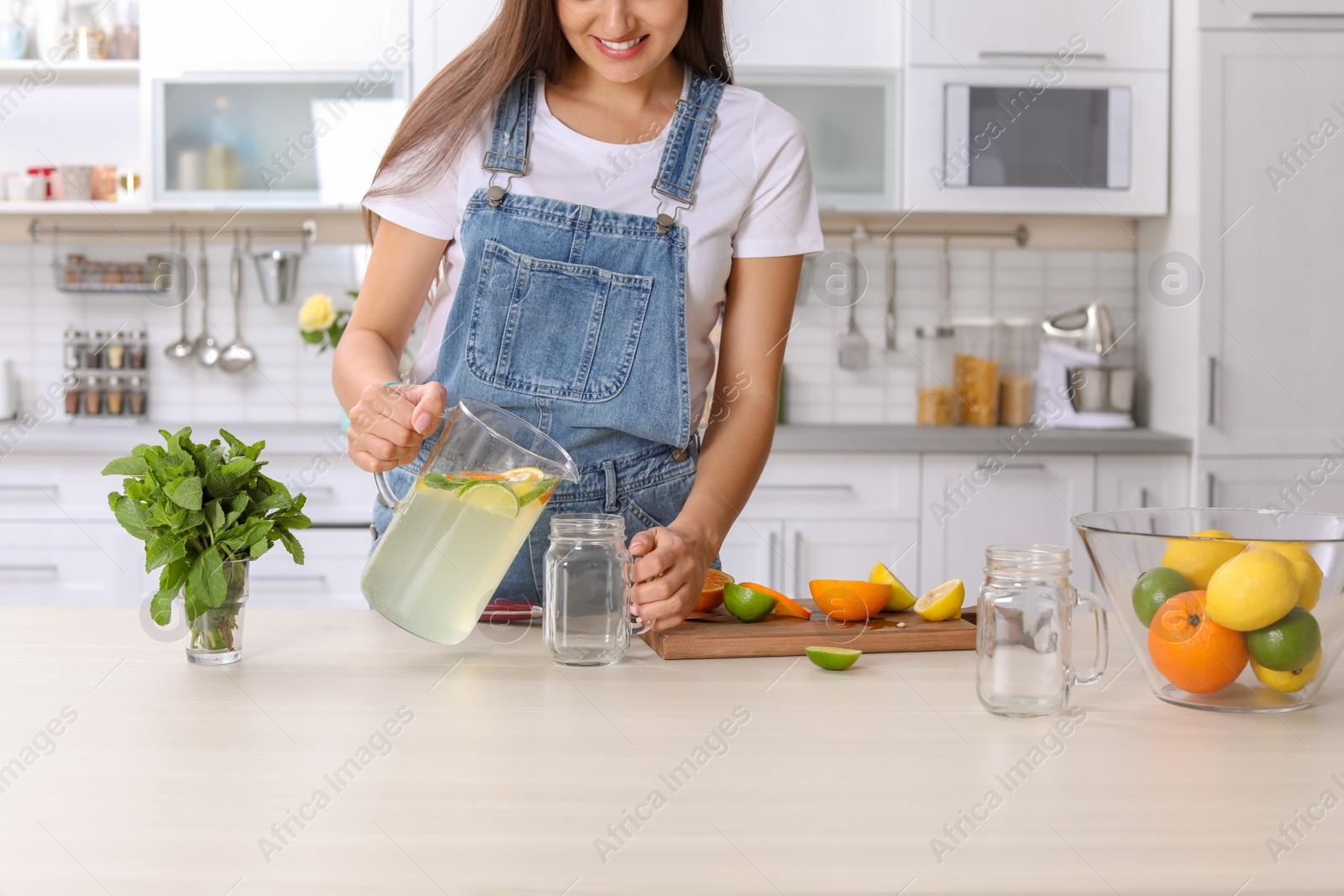 Photo of Young woman preparing lemonade on table in kitchen. Natural detox drink