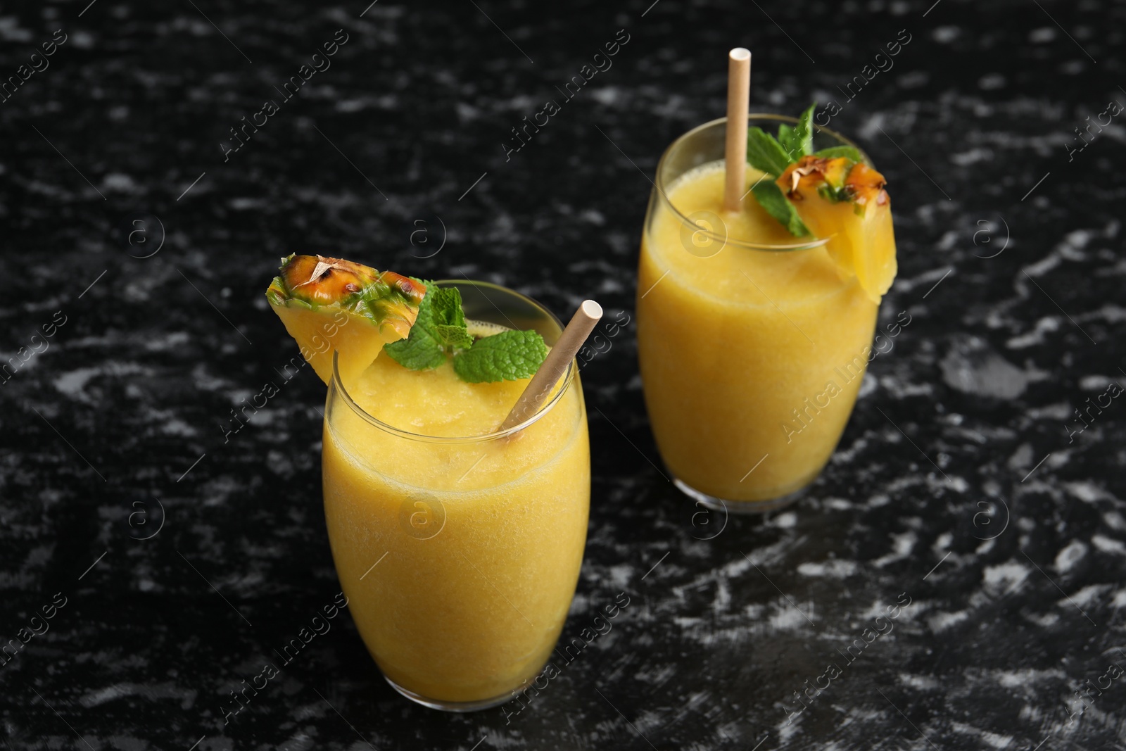 Photo of Tasty pineapple smoothie in glasses on black textured table