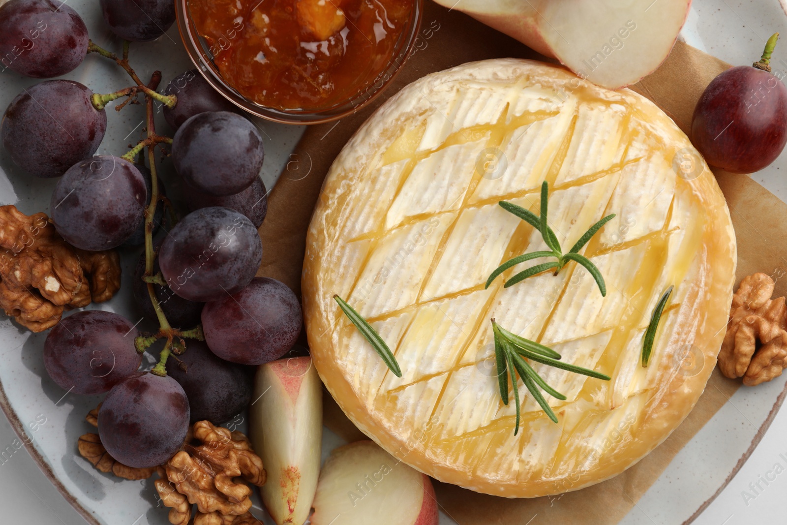 Photo of Tasty baked brie cheese with rosemary, fruits and walnuts on plate, top view