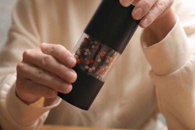 Photo of Woman grinding pepper with shaker at table, closeup