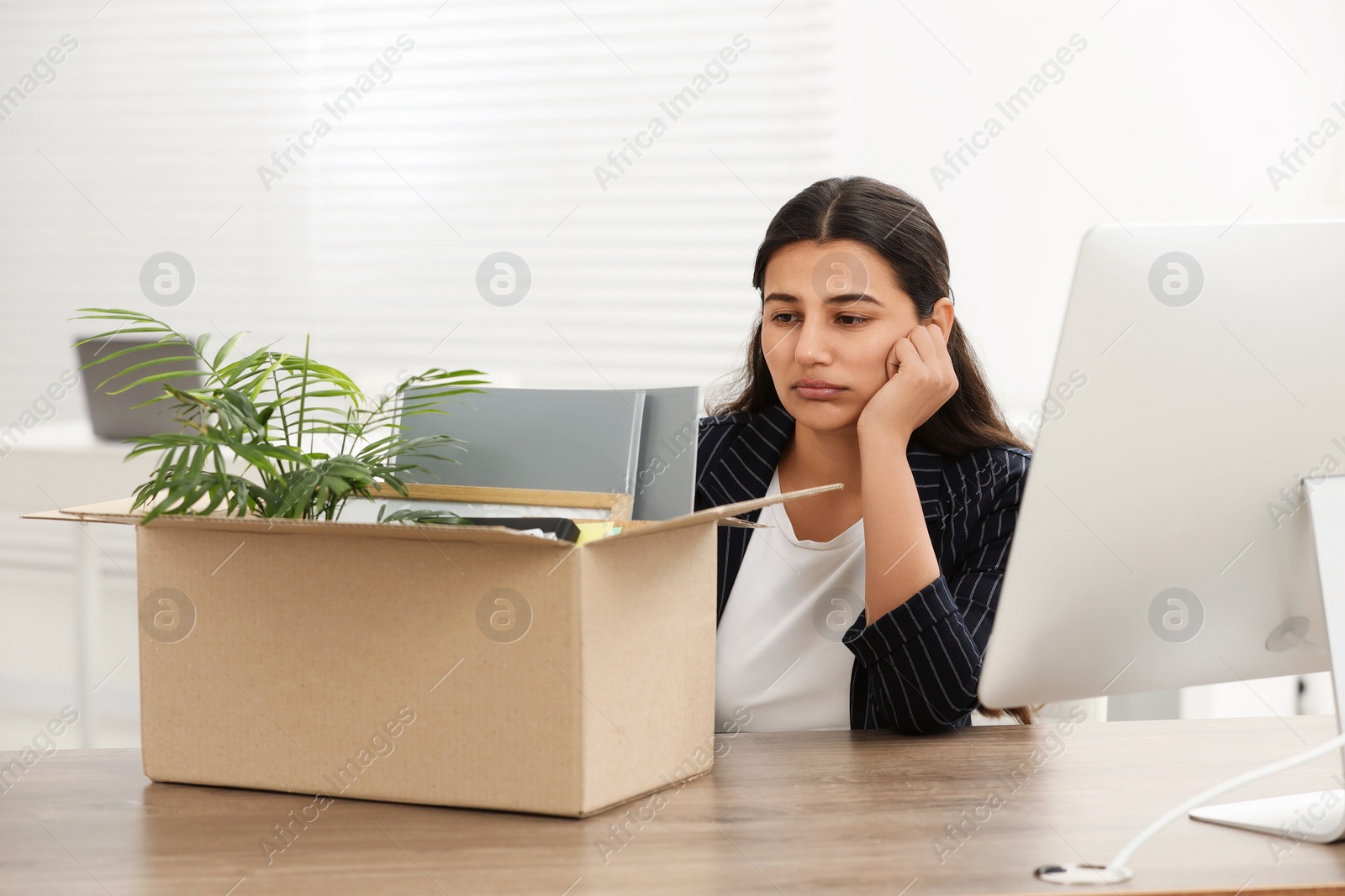 Photo of Unemployment problem. Woman with box of personal belongings at table in office