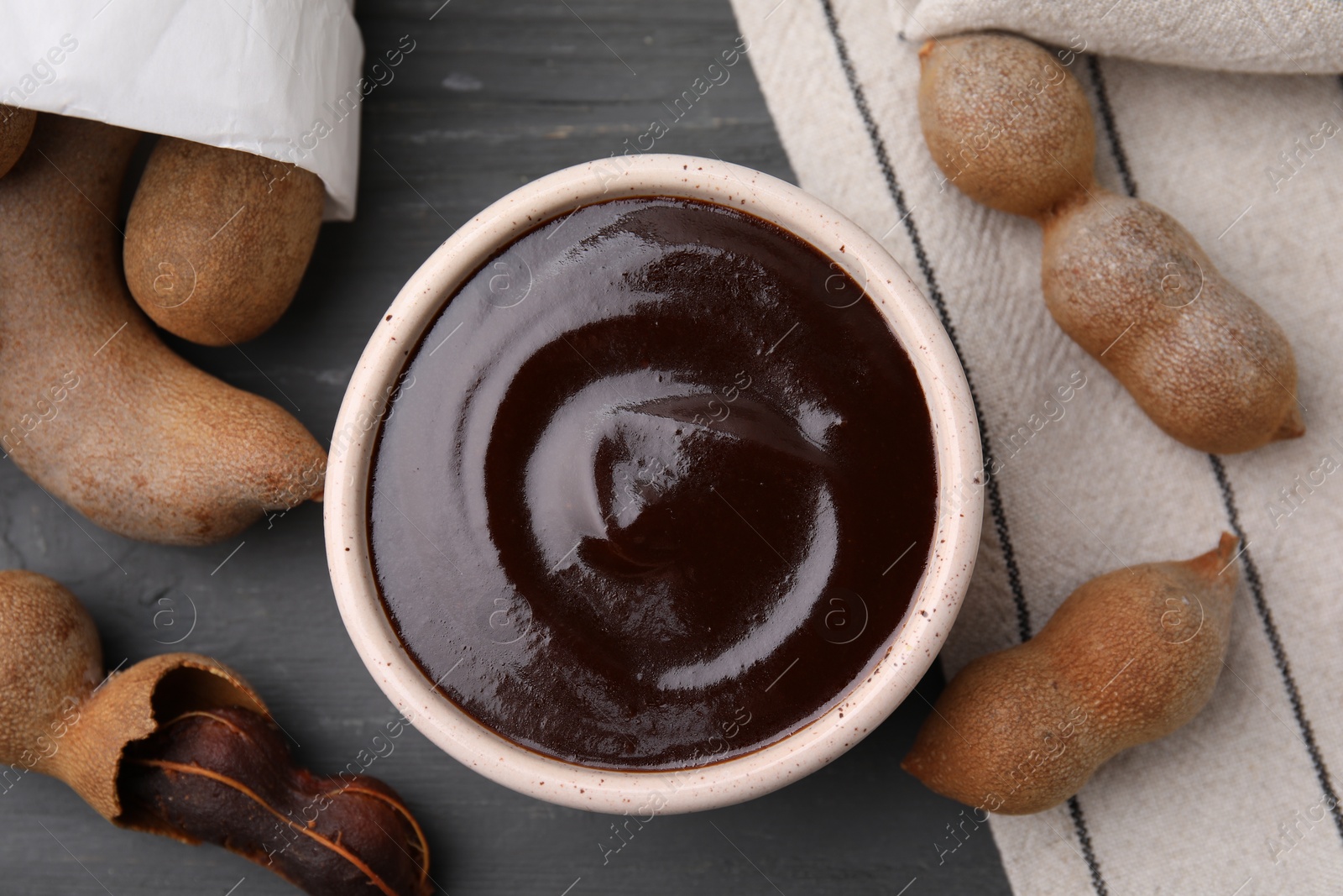 Bowl of tamarind sauce and fresh pods on grey wooden table, flat lay Photo of Bowl of tamarind sauce and fresh pods on grey wooden table, flat lay