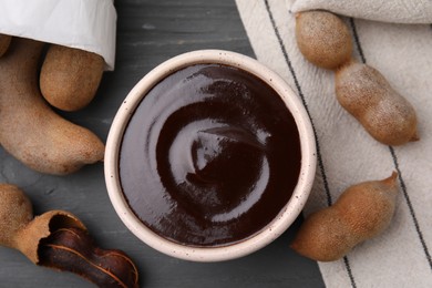 Photo of Bowl of tamarind sauce and fresh pods on grey wooden table, flat lay