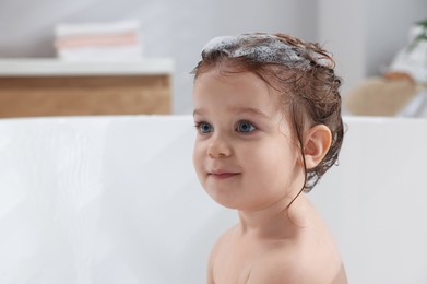 Photo of Cute little girl washing hair with shampoo in bathroom