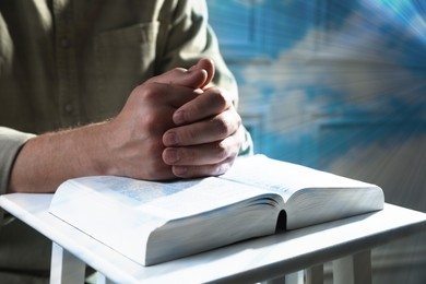 Image of Religion. Christian man praying over Bible at table, closeup