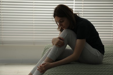 Photo of Sad young woman sitting on bed at home, space for text