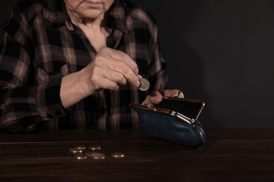 Poor mature woman putting coins into wallet at table, closeup