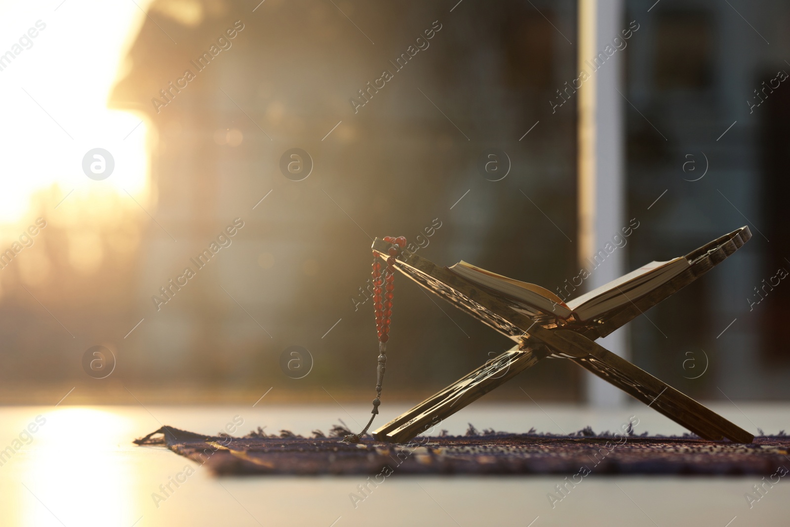 Photo of Rehal with open Quran and Muslim prayer beads on rug indoors. Space for text