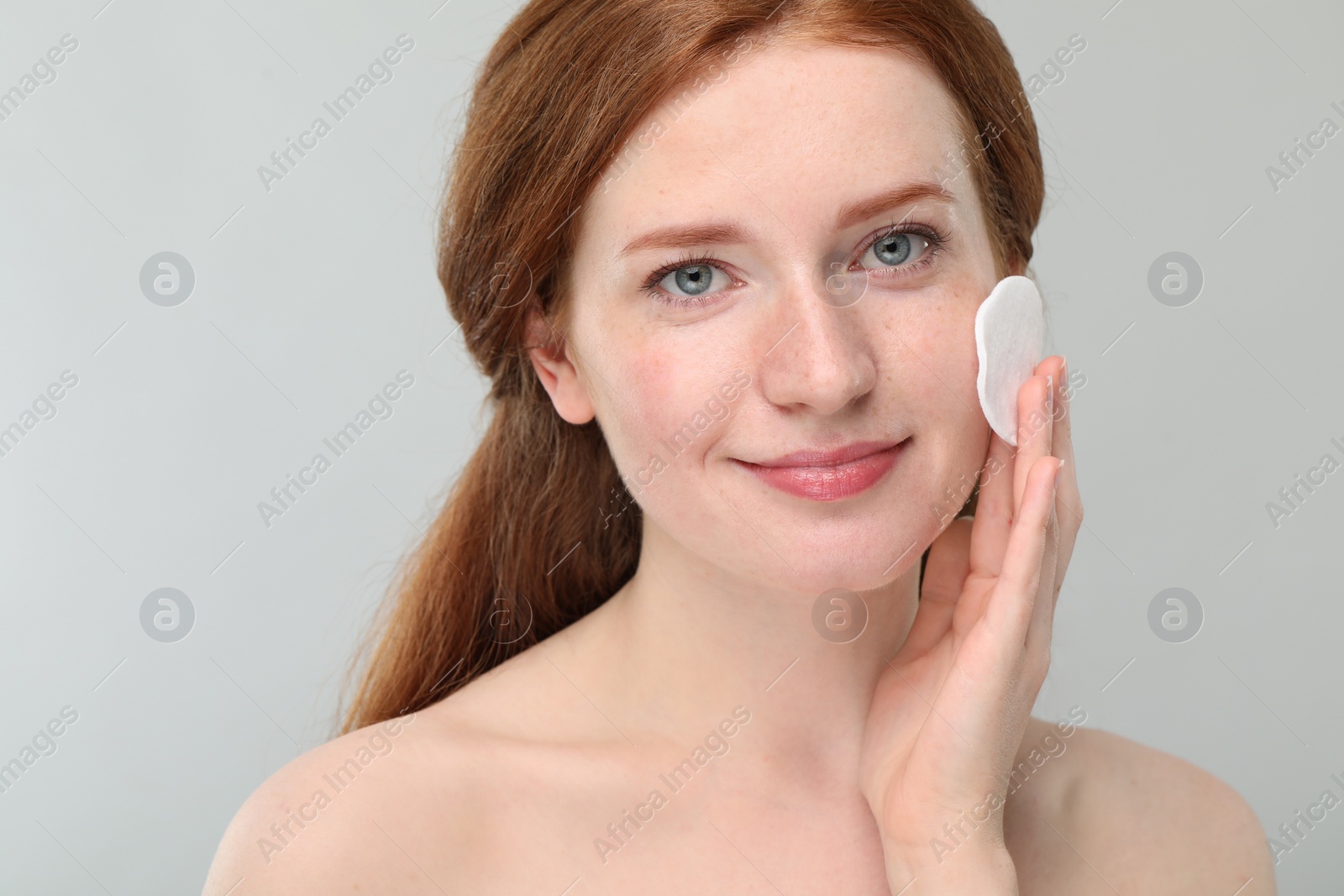 Photo of Beautiful woman with freckles wiping face on grey background