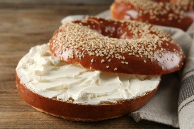 Photo of Delicious bagel with cream cheese on wooden table, closeup