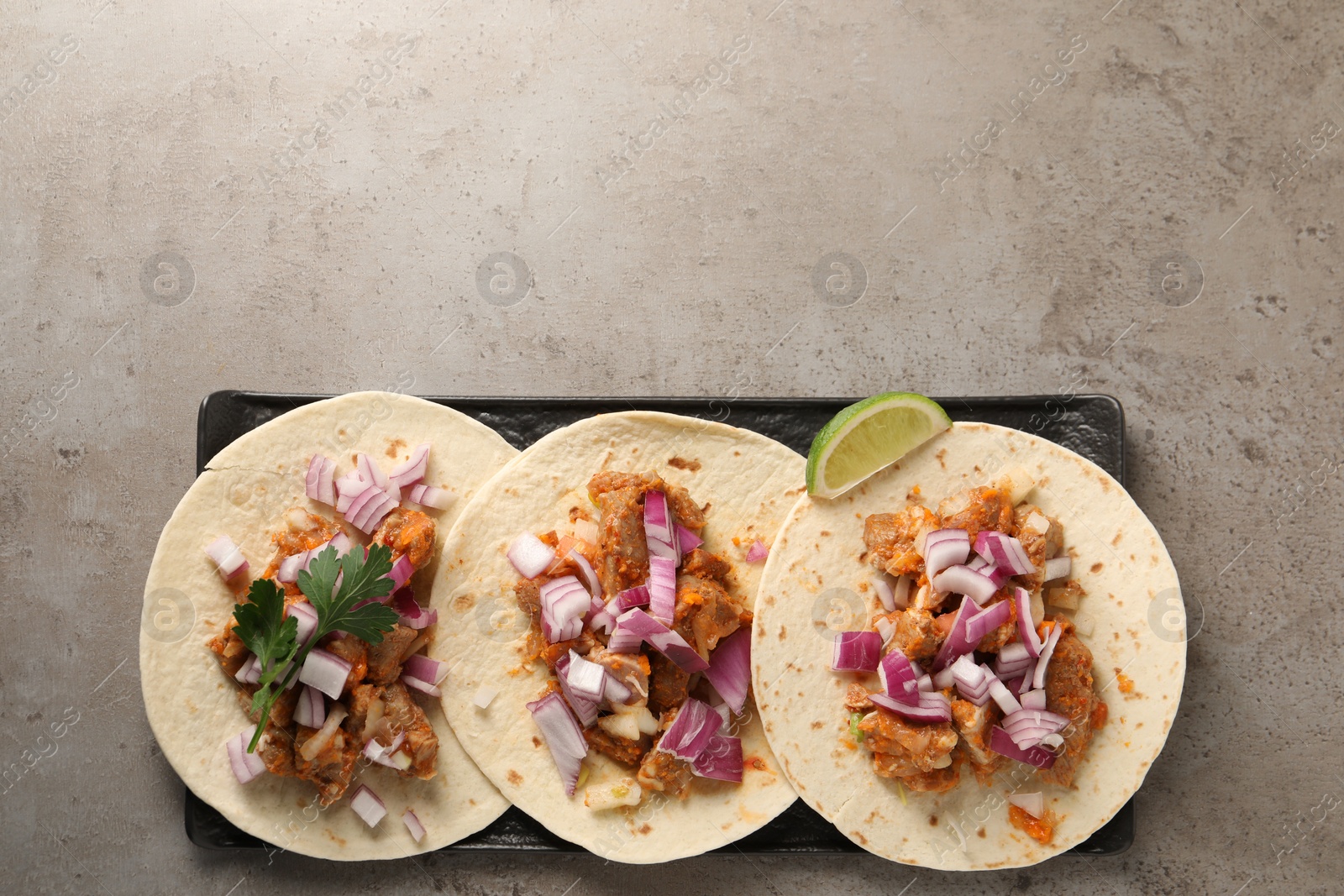 Photo of Delicious tacos with vegetables, meat and lime on grey textured table, top view. Space for text