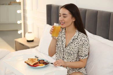 Happy young woman having breakfast on bed at home