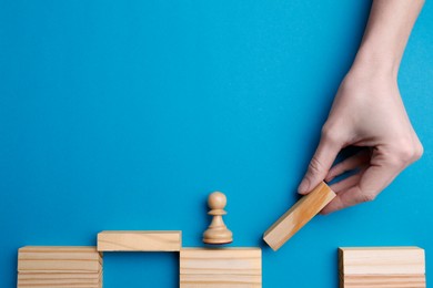Photo of Woman building bridge with wooden blocks on light blue background, top view. Connection and risks concept