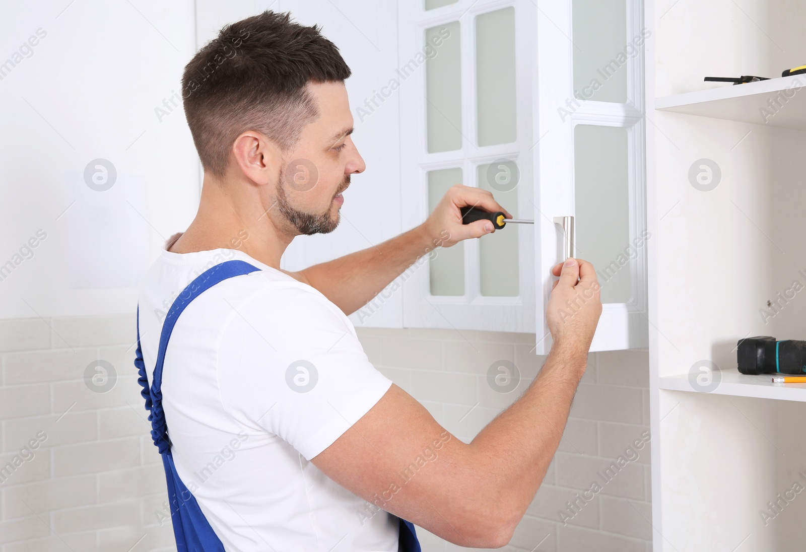 Photo of Worker installing handle of cabinet door with screwdriver in kitchen