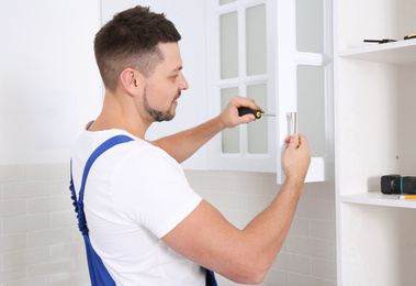 Photo of Worker installing handle of cabinet door with screwdriver in kitchen
