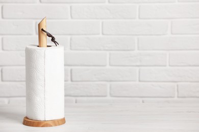 Photo of Holder with roll of paper towels on white wooden table near brick wall. Space for text