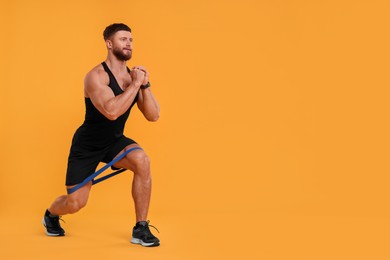 Photo of Young man exercising with elastic resistance band on orange background. Space for text