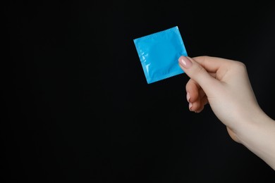 Photo of Woman holding condom on black background, closeup. Space for text