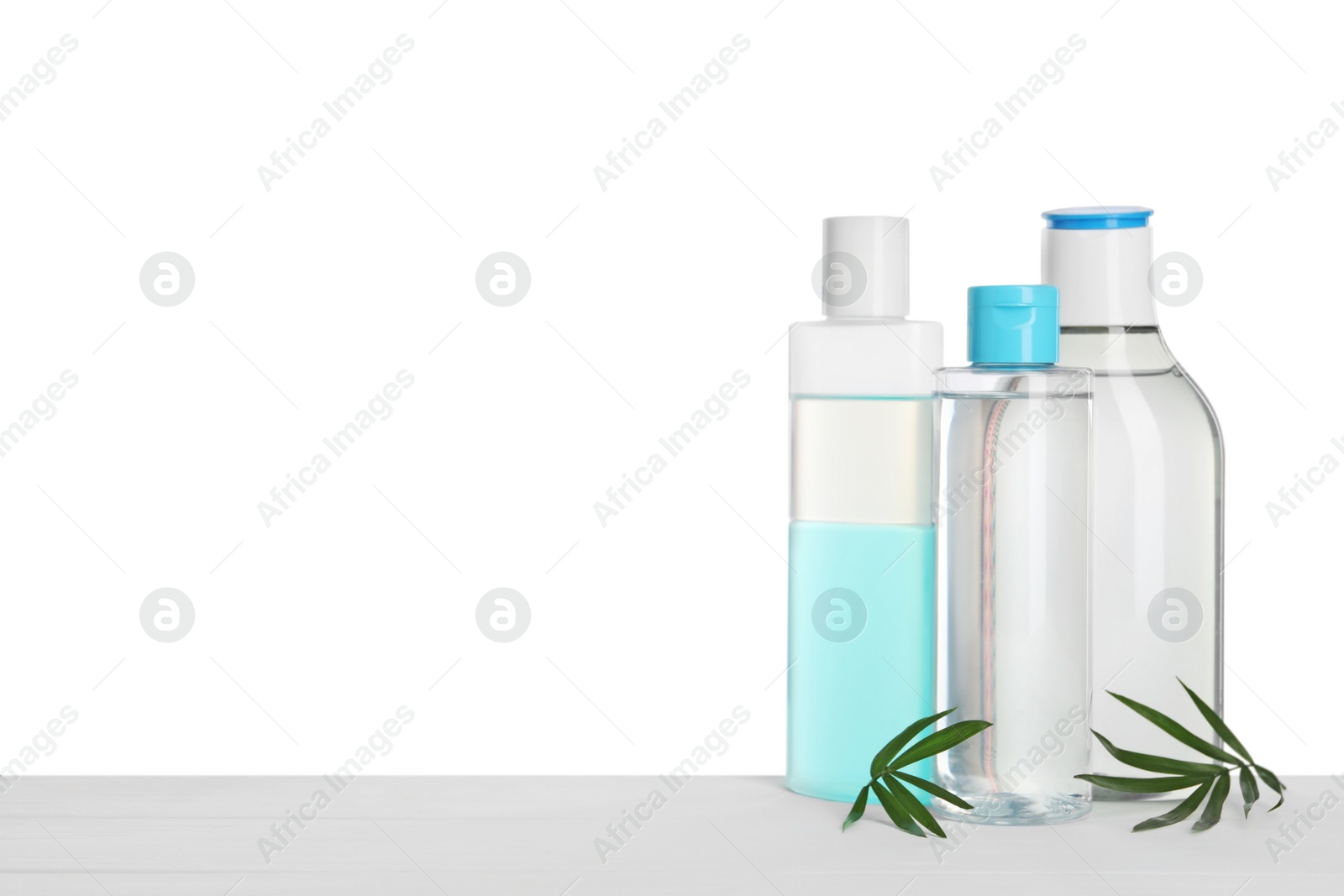 Photo of Micellar water in bottles on table against white background. Space for text