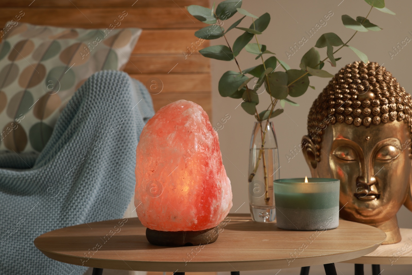 Photo of Beautiful Himalayan salt lamp, golden Buddha sculpture and decor on wooden tables in living room