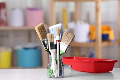 Photo of Glass jar with paint brushes and tray on table in workshop. Space for text